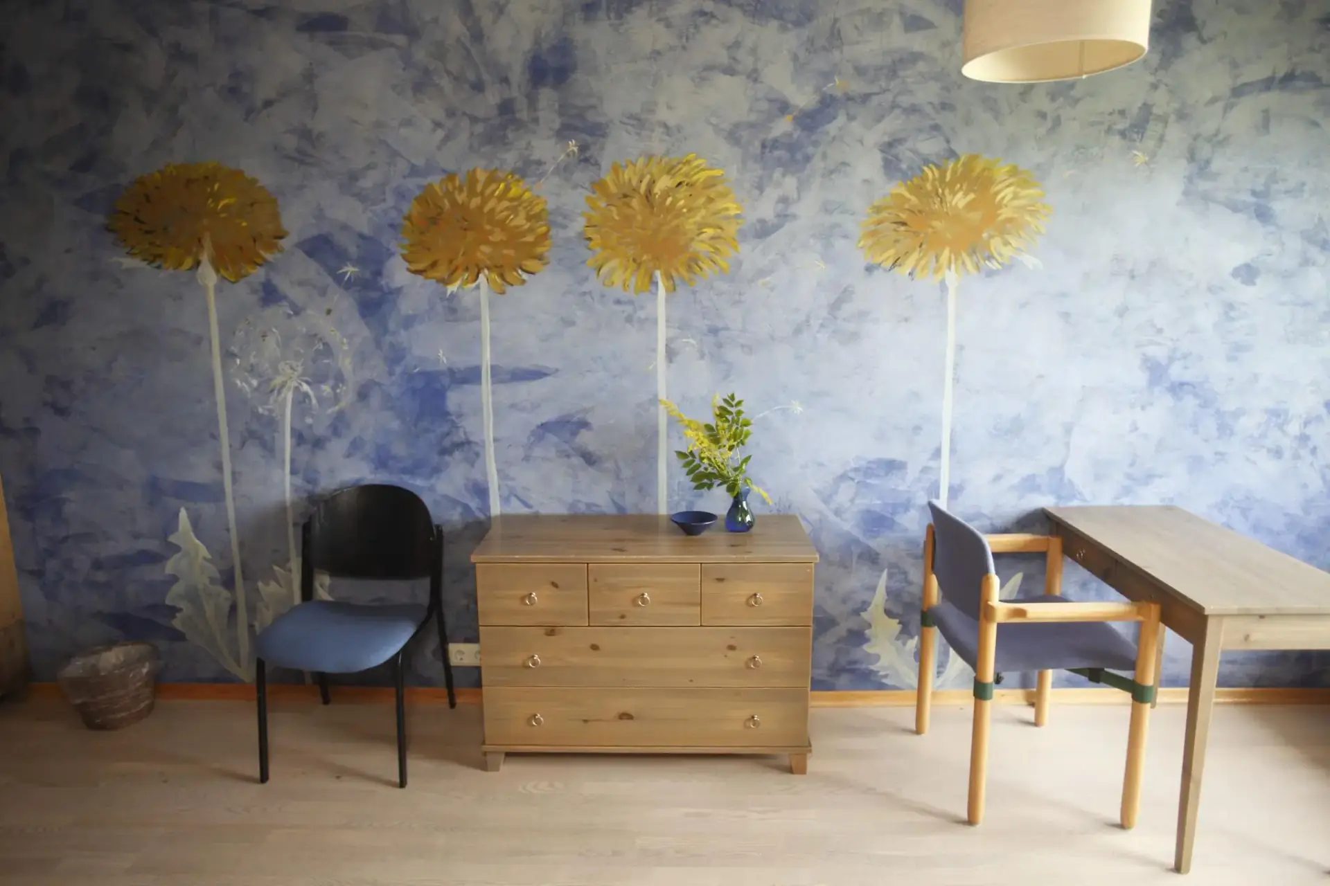 Room with a blue wall painted with tall dandelions, chest of drawers and desk