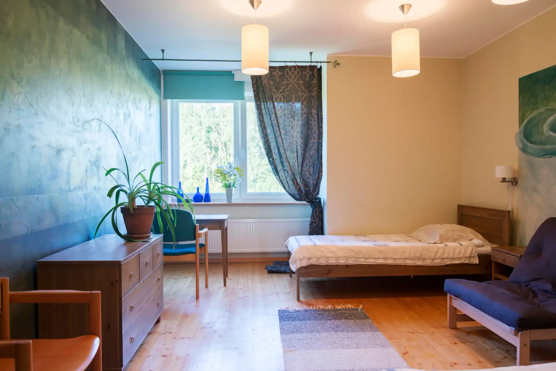 Sea-green room with a painted wall, single bed and desk by the window