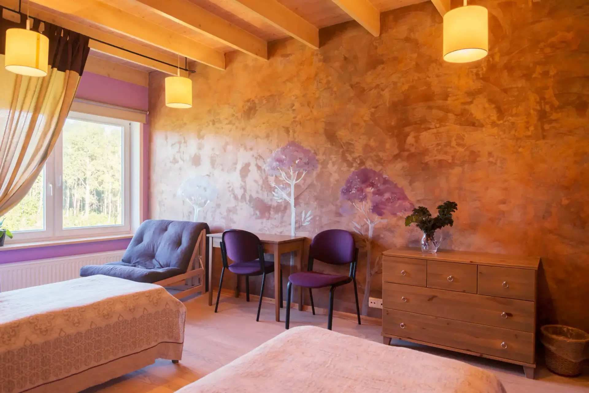Twin room with painted trees on an ochre wall and a small table